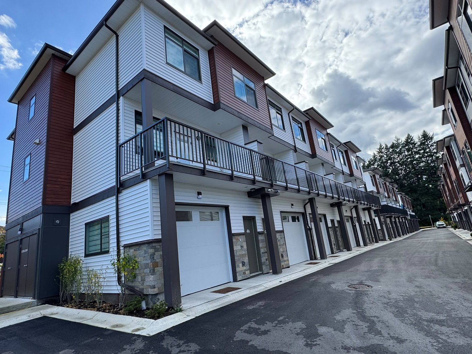 Completed attached townhomes with garages, upper balconies and a paved access lane.