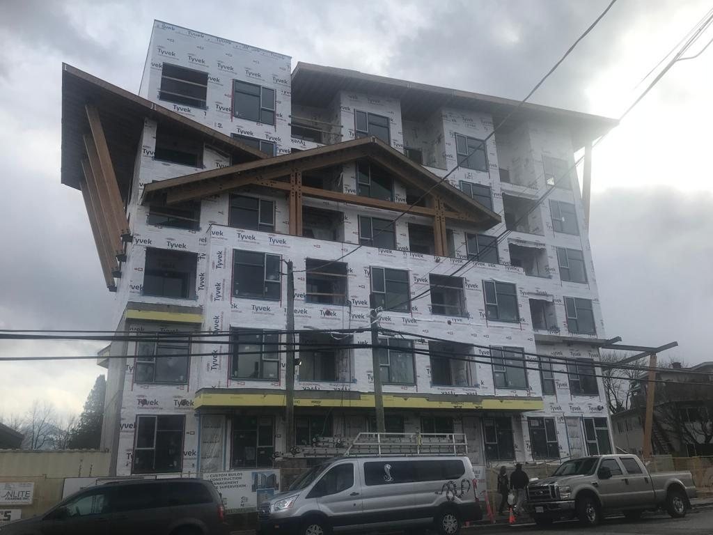 Multi-storey building wrapped in weather barrier, with windows and projecting balconies.