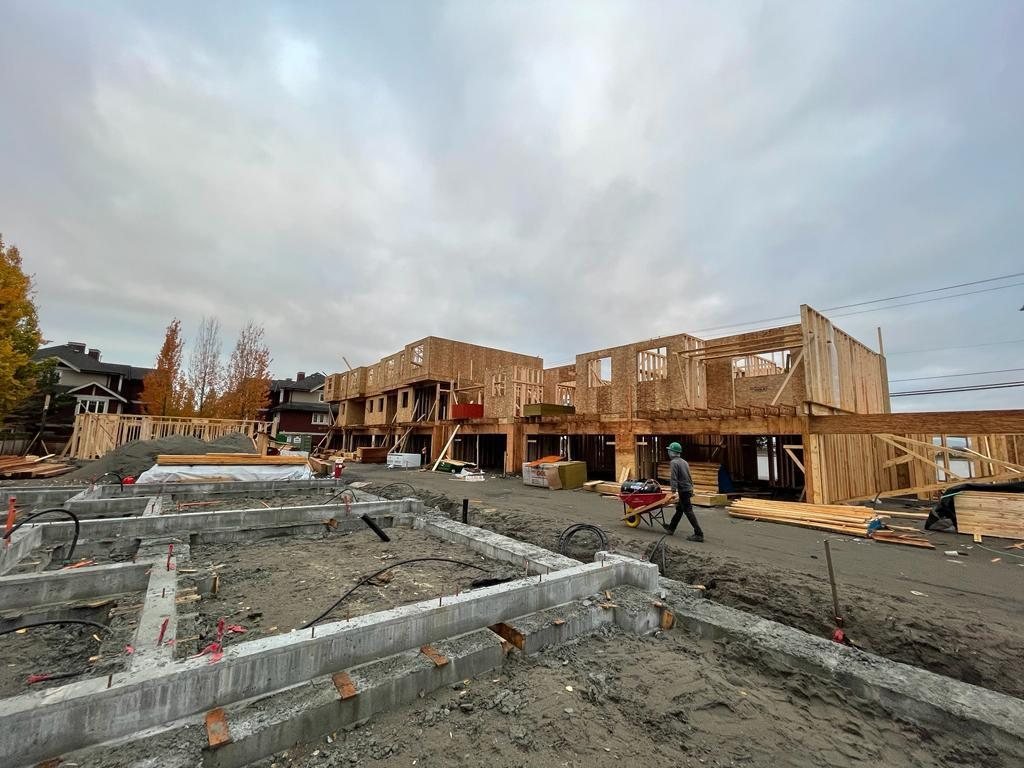Wood wall framing under way beside concrete foundation walls, with a worker moving materials across the site.