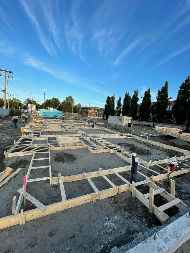 Timber foundation formwork laid out across an excavated site, with service pipes rising near the foreground.