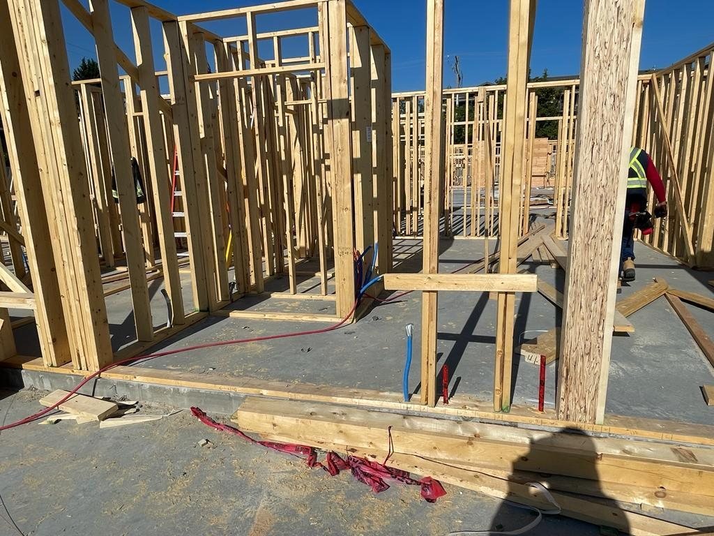 Interior wood wall framing with door openings and red and blue service lines crossing a concrete floor.