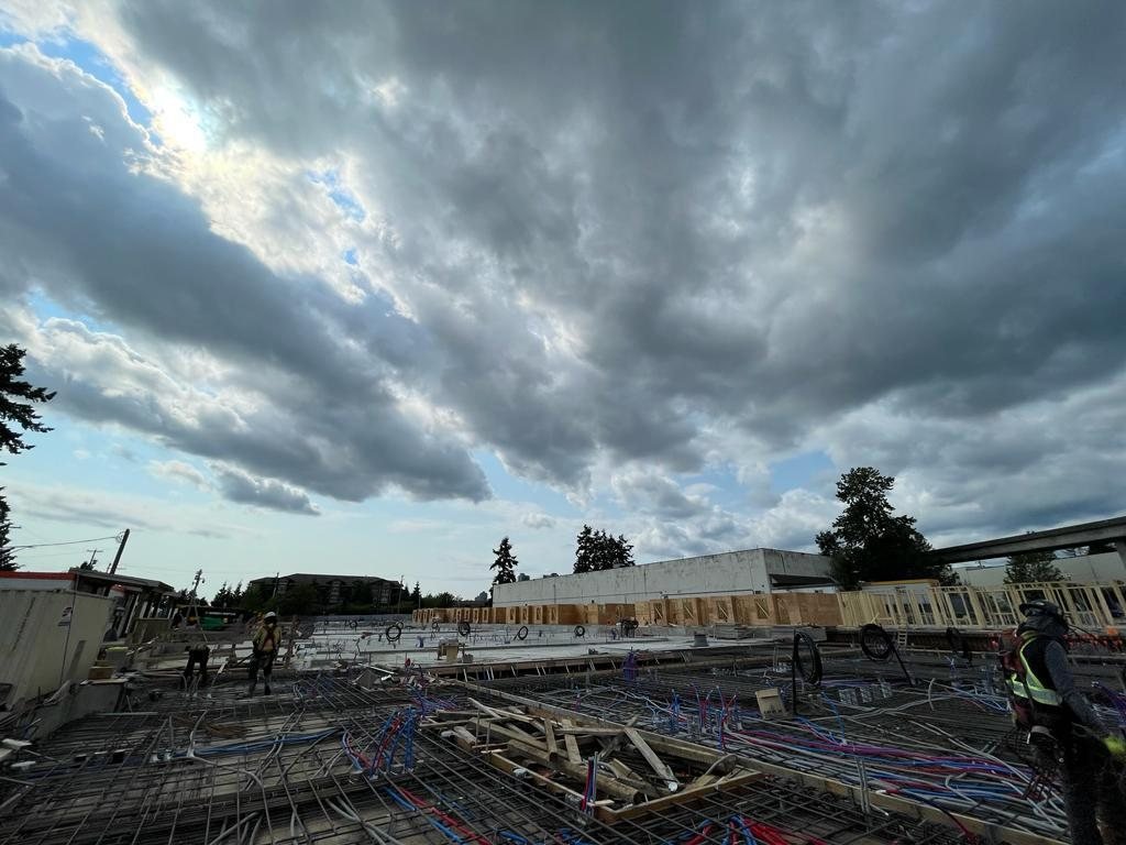 Concrete slab work with reinforcing mesh, coloured service lines and perimeter forms beneath a cloudy sky.