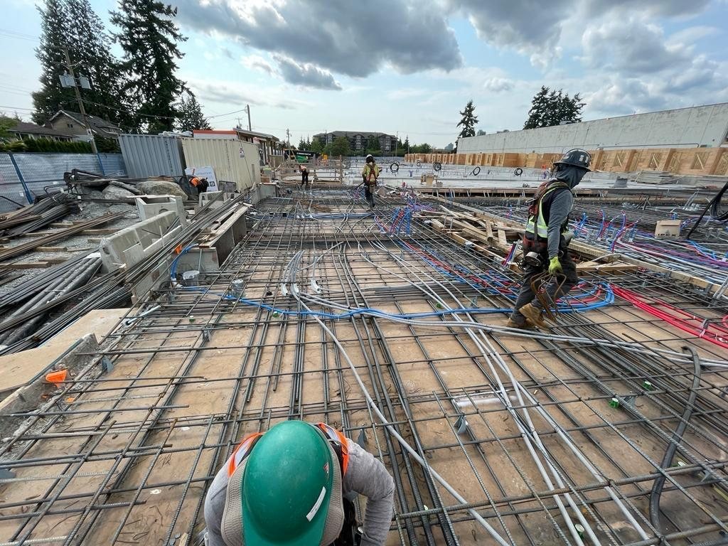 Workers beside reinforcing steel and coloured service lines laid across a large concrete floor area.