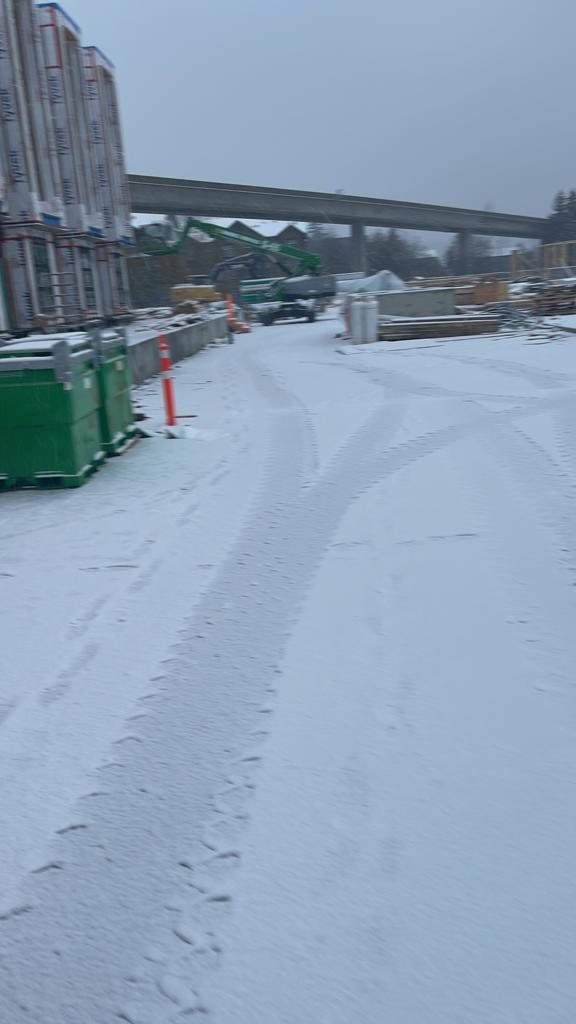 Snow-covered construction access lane between wrapped building materials and active work areas.