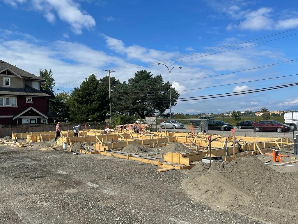 Several workers beside timber foundation forms, with lumber and material areas staged across a residential site.