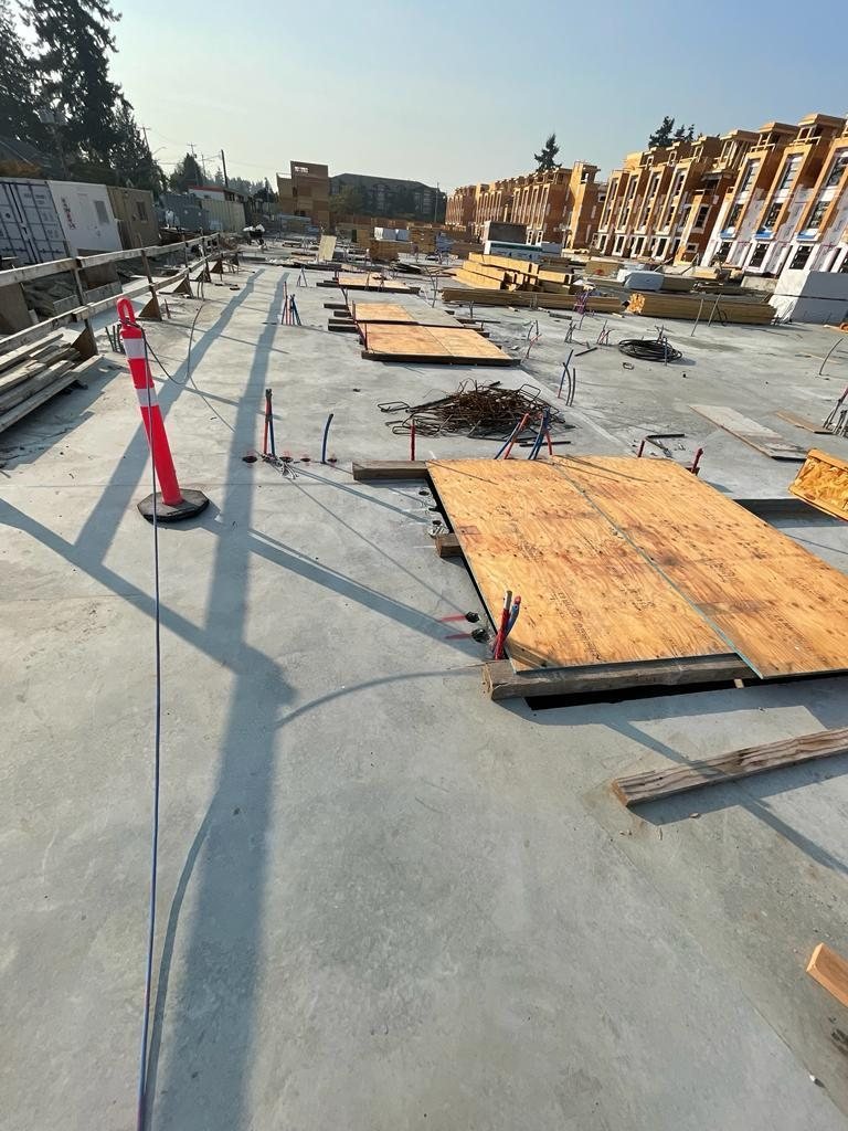 Concrete floor with plywood sheets protecting selected areas, service pipes and stacked lumber near framed townhomes.