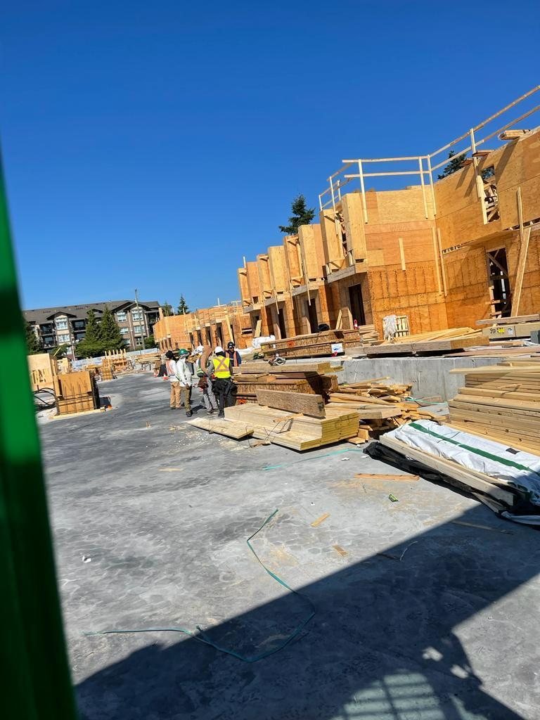 Workers standing beside lumber stacks on a concrete floor next to multi-storey wood framing.