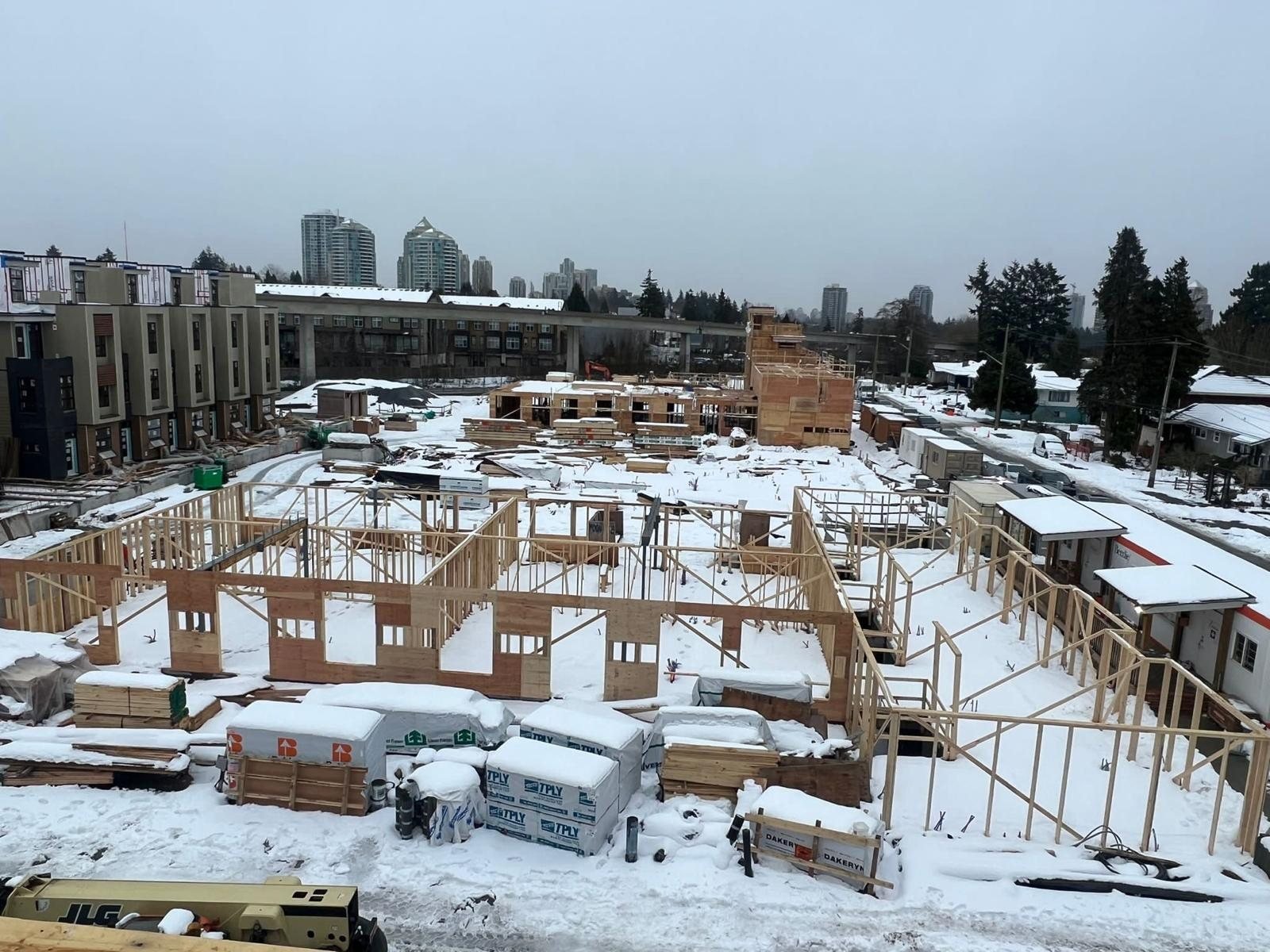 Snow-covered multi-unit construction site with wood framing and stacked materials.