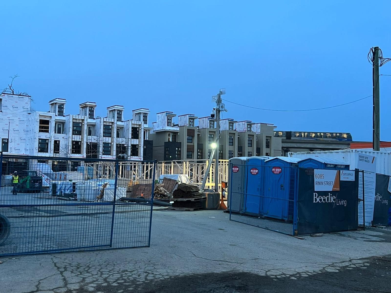 Street-side view of a multi-unit building under construction behind temporary fencing.
