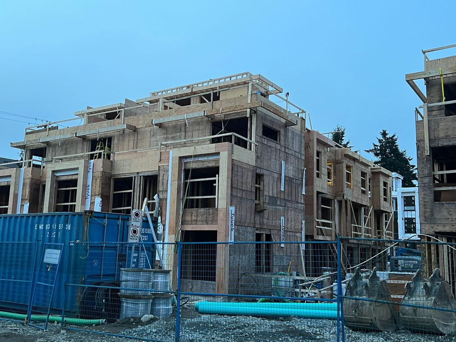 Multi-storey wood building wrapped in structural panels beside a blue construction fence.