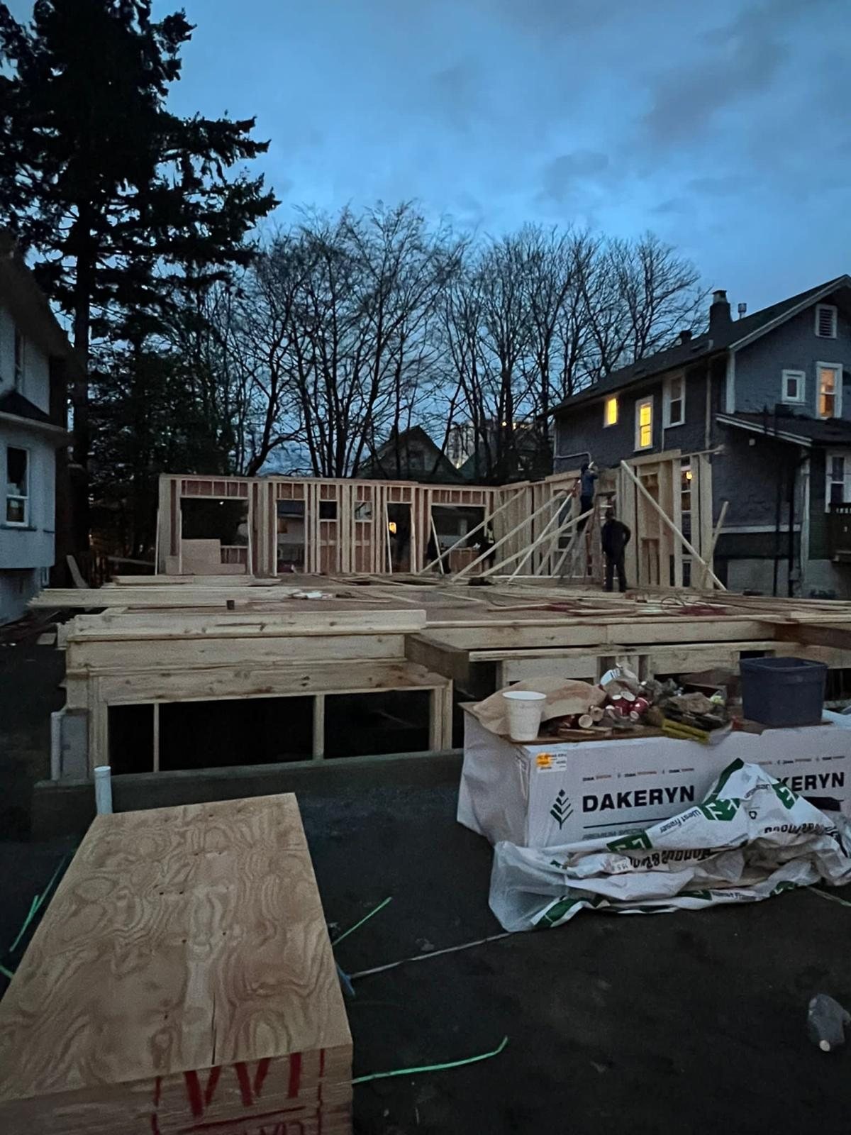 Low-rise wood framing and sheathing on a construction site bordered by trees.