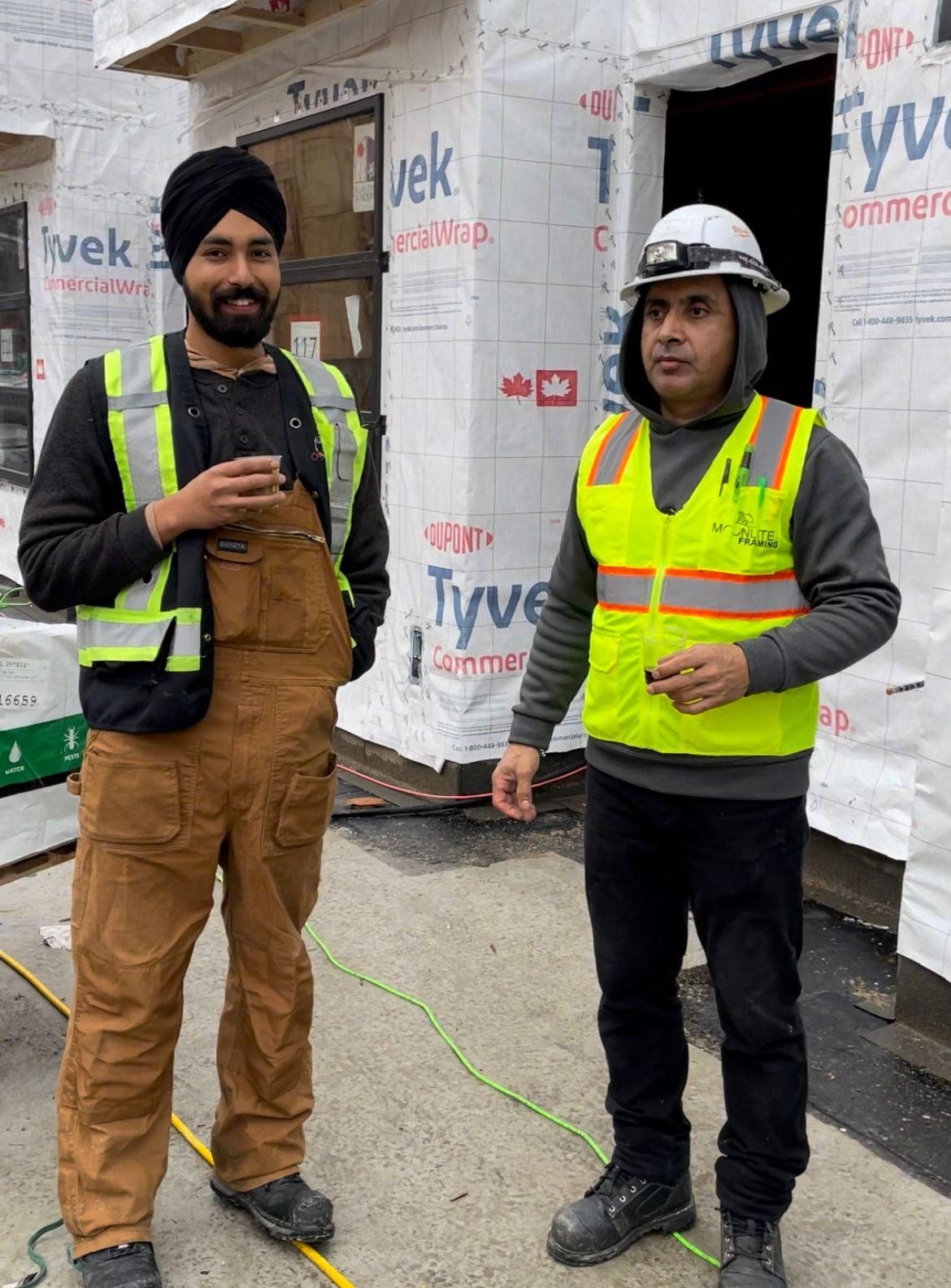 Two construction workers in high-visibility clothing standing inside a framed building.