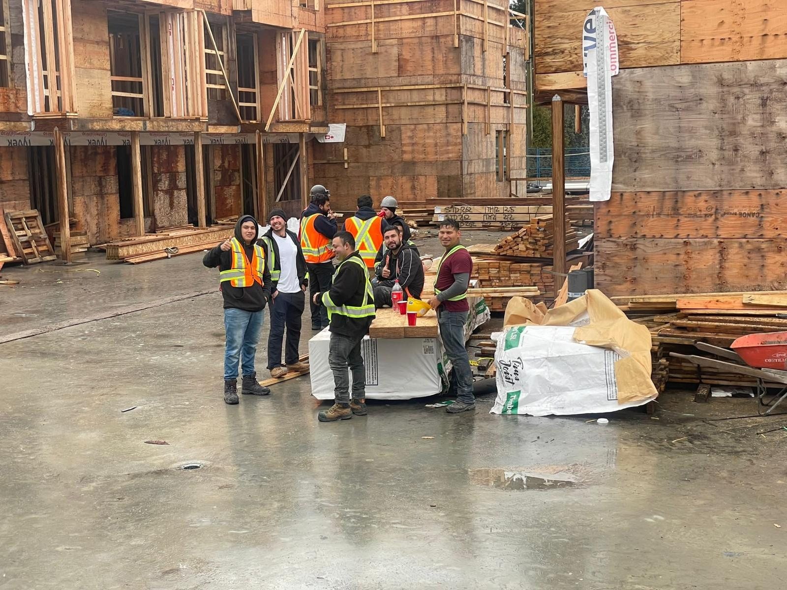 Construction workers moving materials across a concrete floor beside wood wall framing.