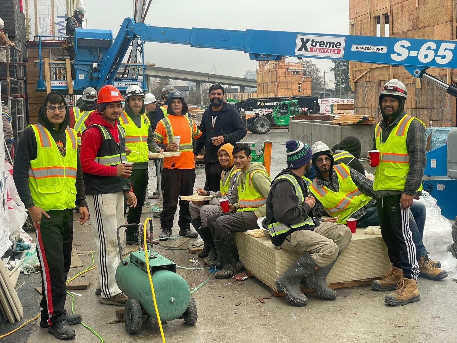 Group of construction workers in safety gear beside a material lift and wood framing.