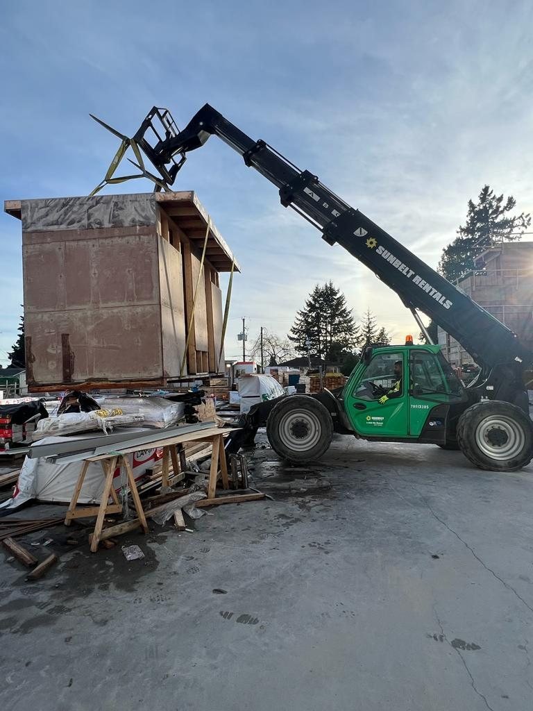 Telehandler boom raised beside a multi-storey wood-framed building.