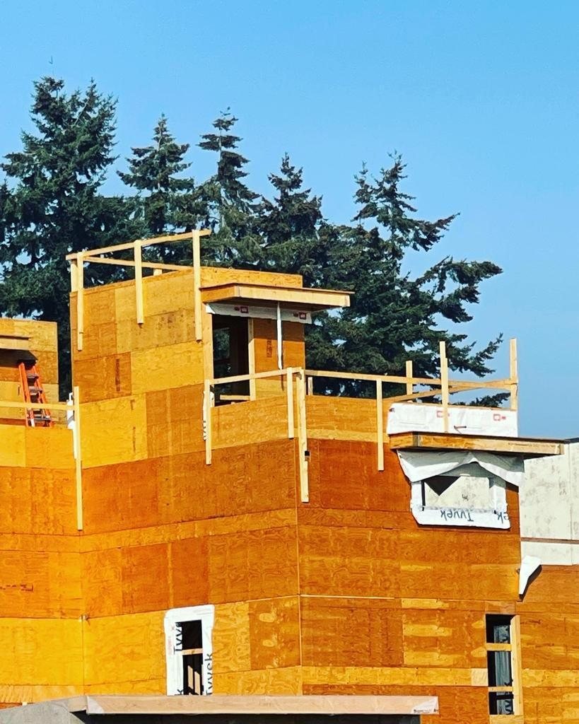 Multi-storey wood-frame exterior covered with structural panels and weather protection.
