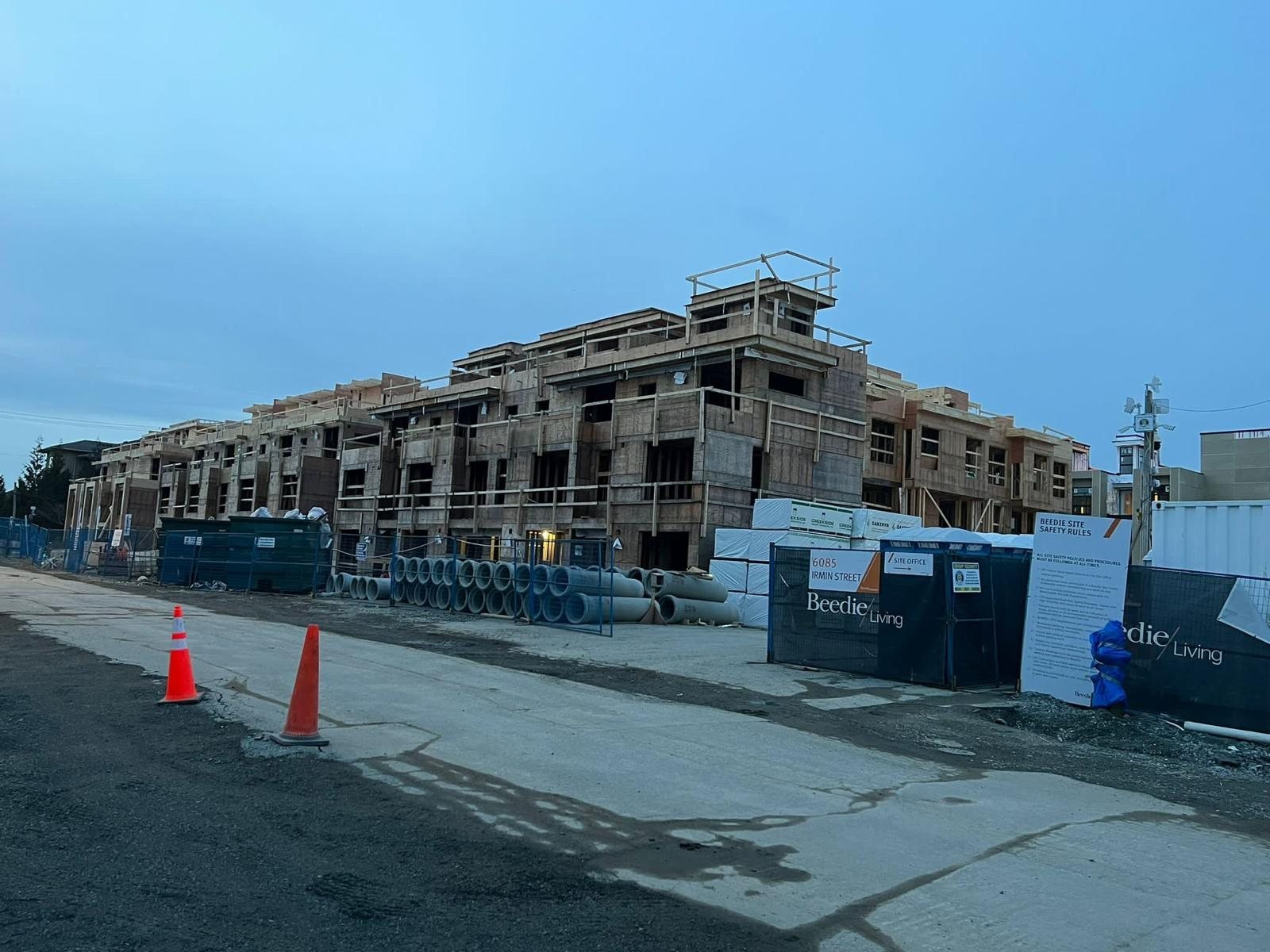 Multi-family wood construction behind temporary fencing and site storage containers.