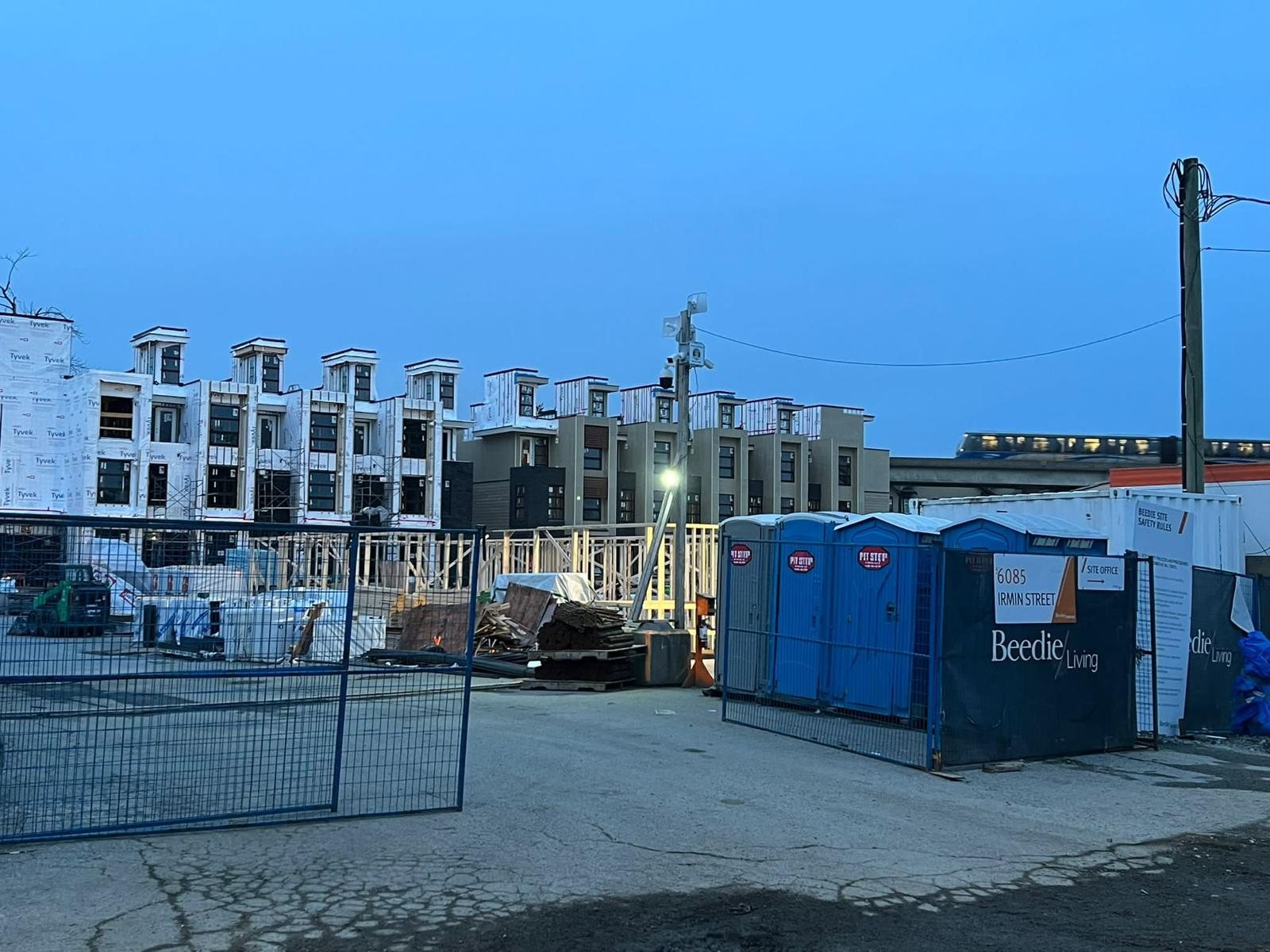 Street-side view of a multi-storey wood-frame building behind a secured construction fence.