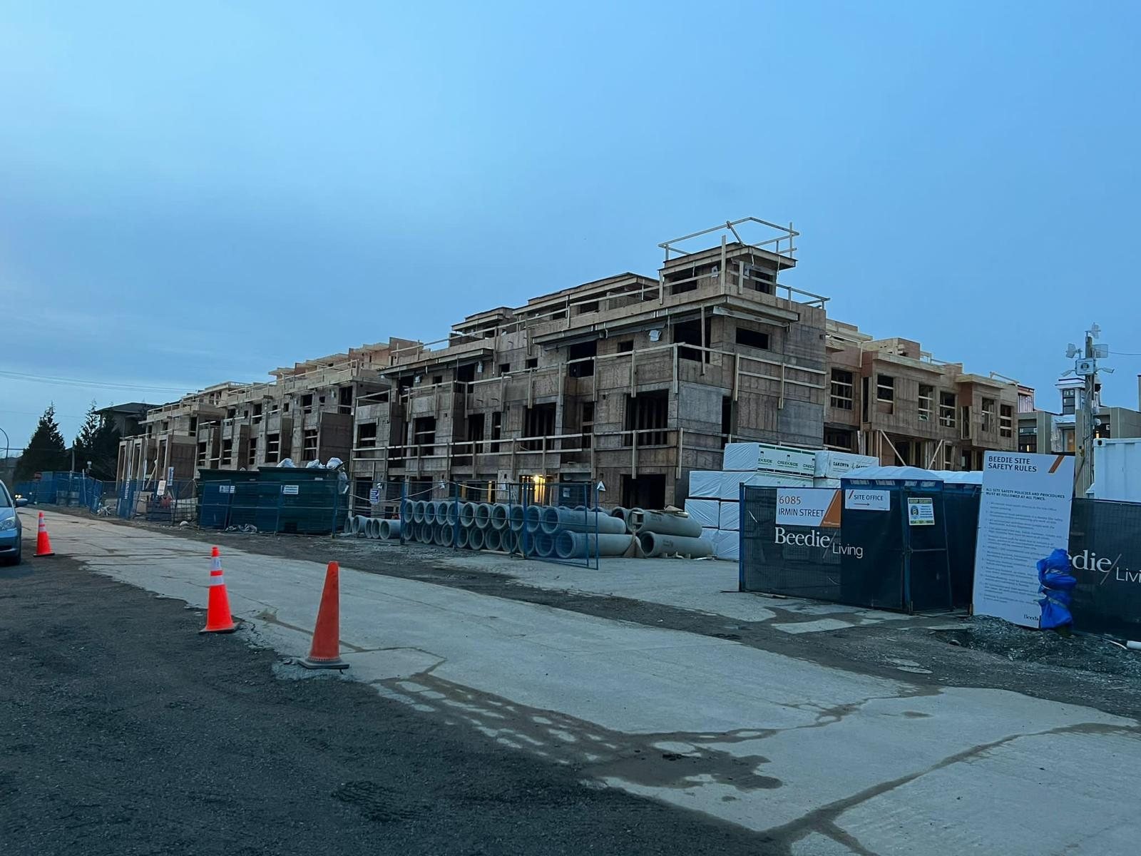 Wide view of several wood-framed building sections behind cones and temporary fencing.