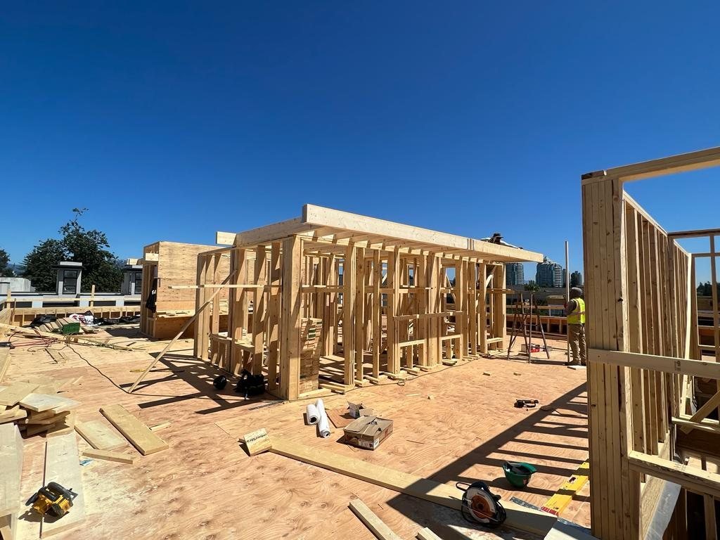 Open wood wall framing and floor platform beside a neighbouring multi-unit building.