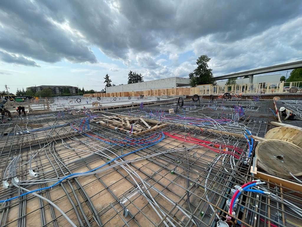 Workers beside reinforcing steel and service lines spread across a slab work area.
