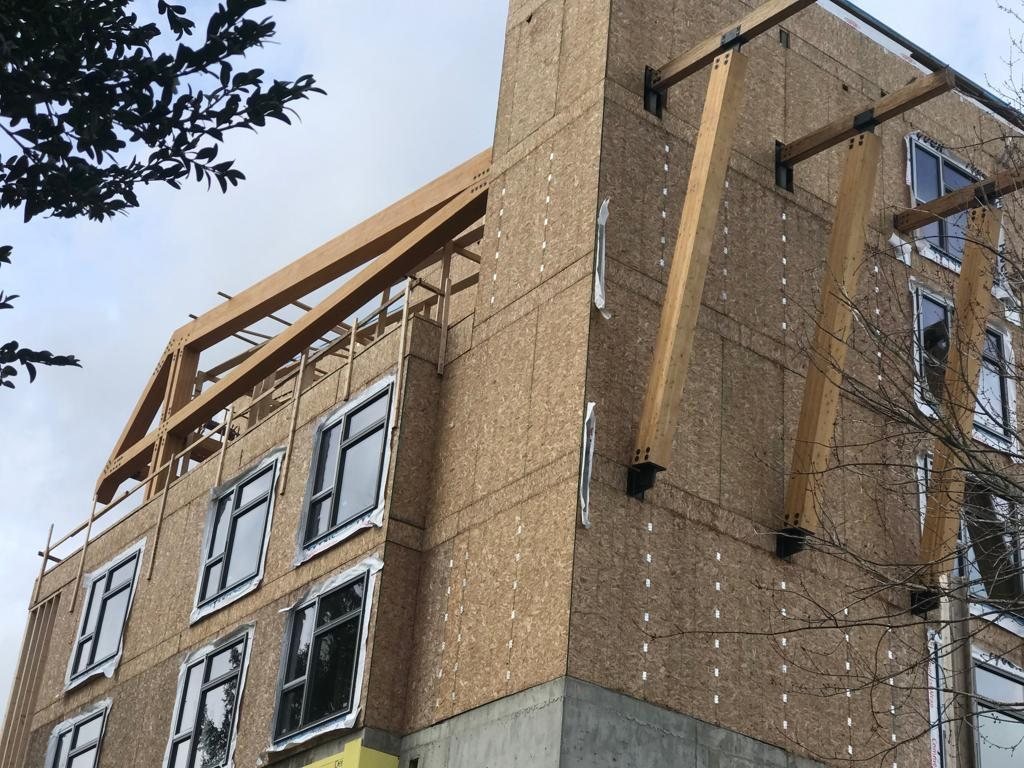 Scaffold and protective mesh beside a multi-storey wood building covered in panels.