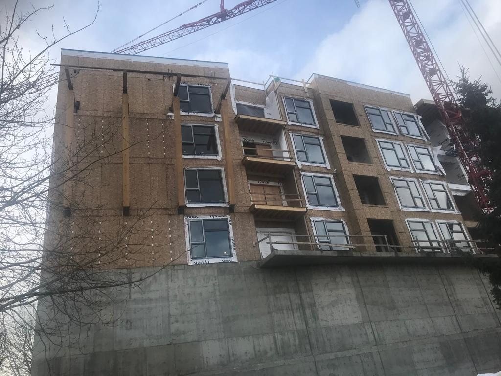 Wood-framed upper levels above a concrete base wall on a multi-storey building.