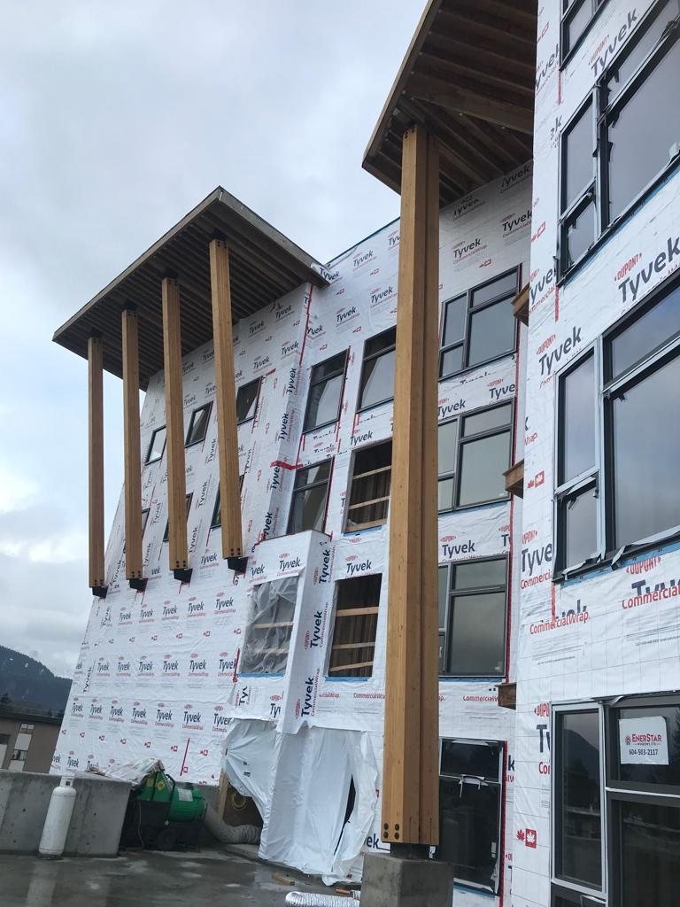 Projecting timber canopy supports beside windows on a wrapped exterior wall.