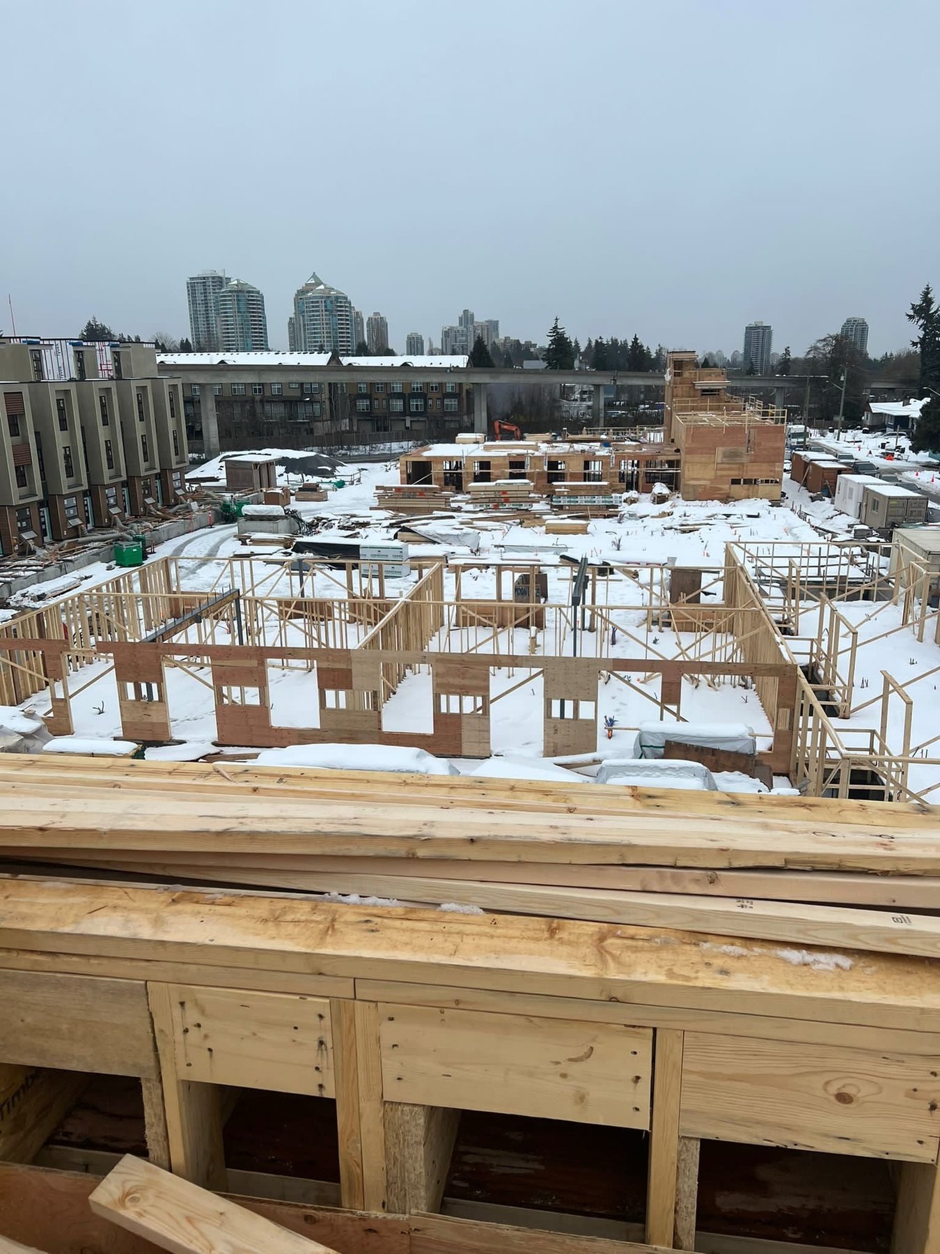 Snow-covered multi-family building site with stacked framing materials.