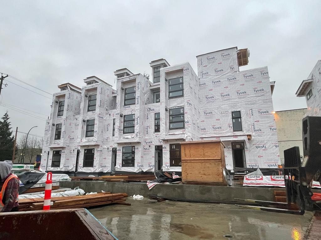 Multi-storey residential building with weather barrier and lumber staged at ground level.