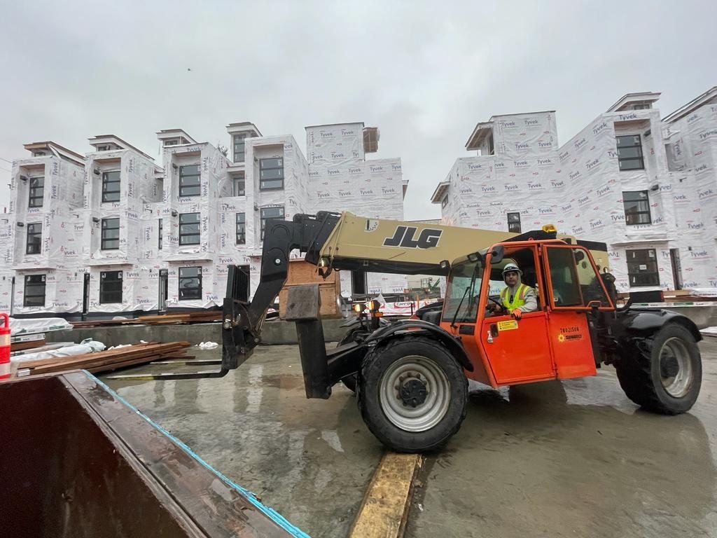 Telehandler and lumber near a multi-storey building covered in weather barrier.