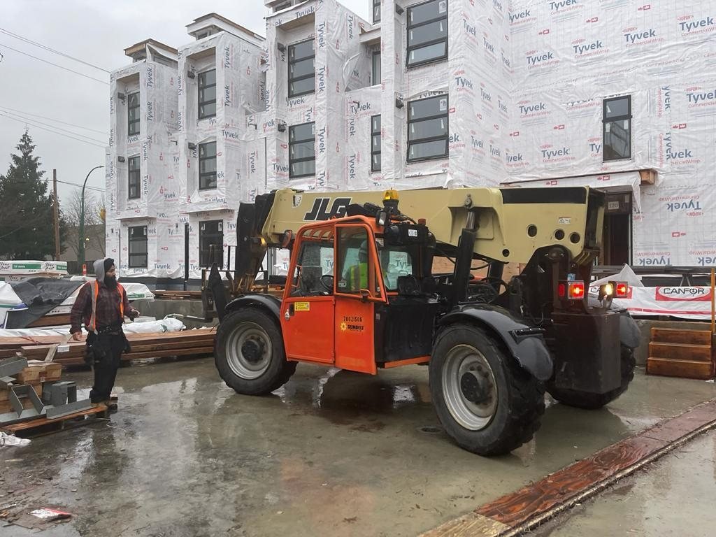 Telehandler carrying framing materials beside multi-unit construction.