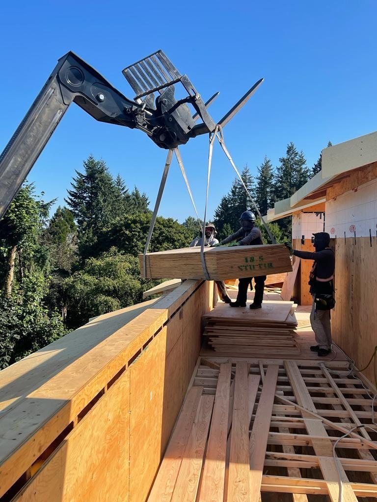 Telehandler lifting materials beside timber roof framing and a building edge.