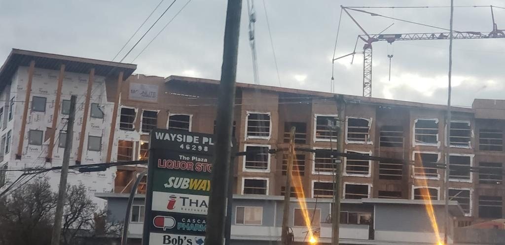 Multi-storey residential construction viewed across a street with retail signs nearby.