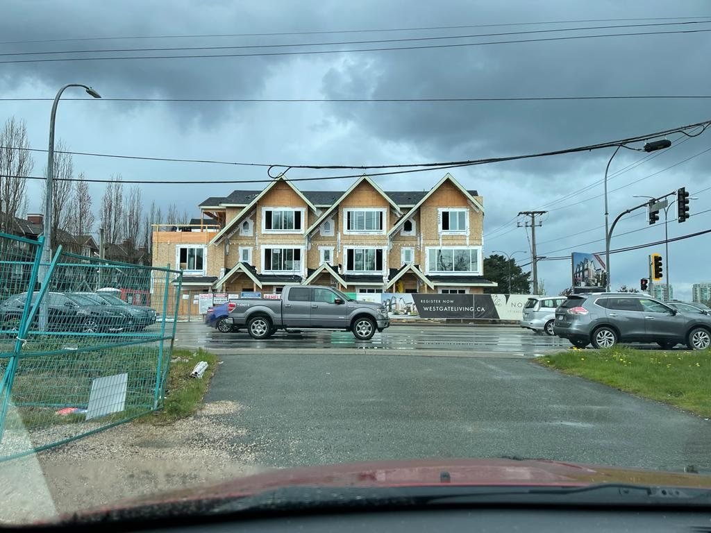 Roadside view of attached homes under construction behind a temporary fence.