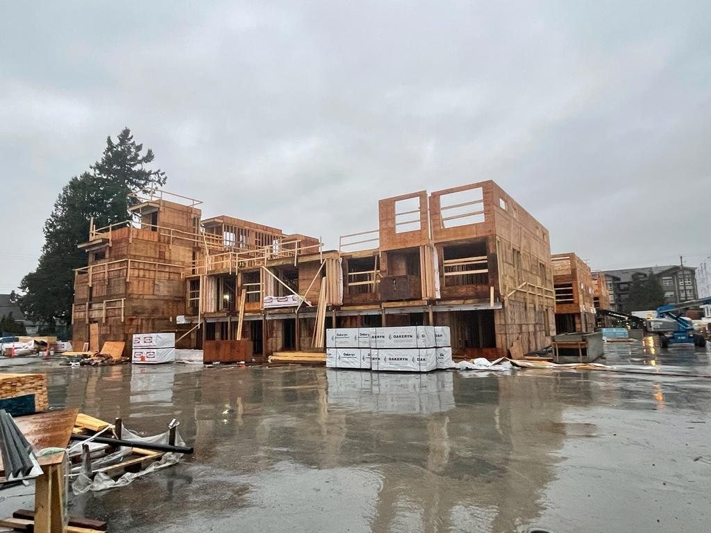 Wood-framed residential building and concrete work area beneath cloudy skies.