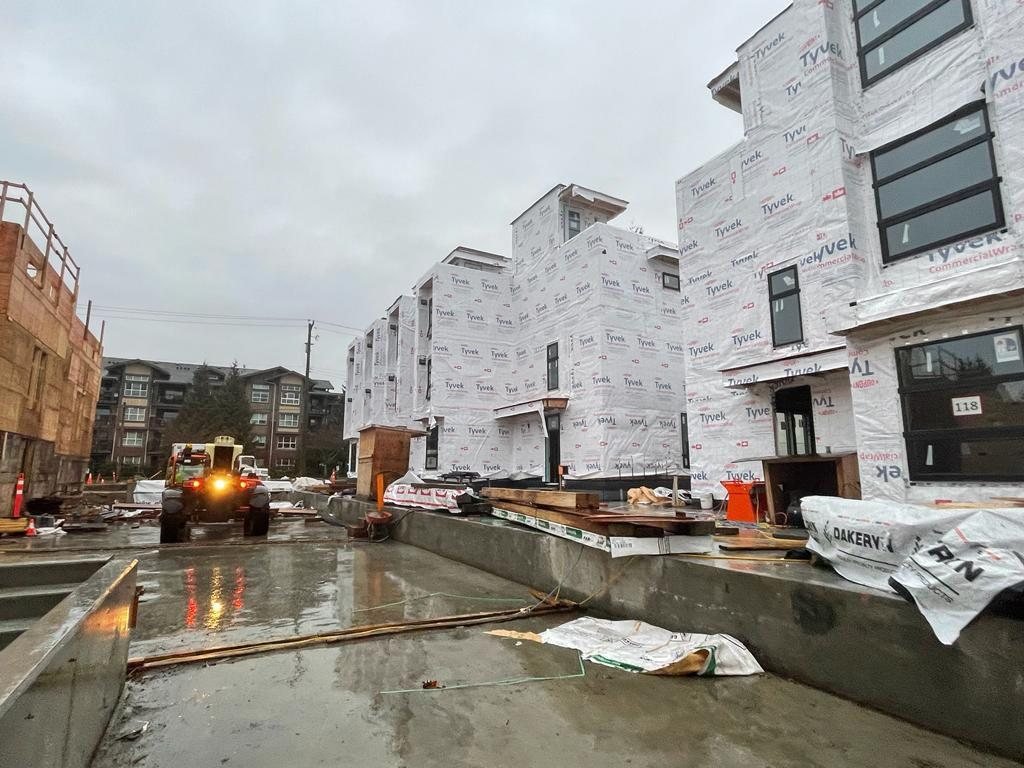 Rainy construction site with wrapped residential buildings and materials at ground level.