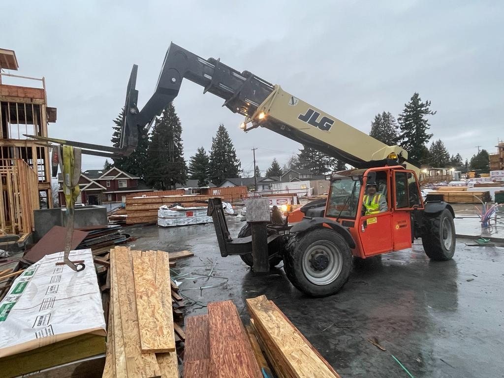 Telehandler moving a lumber package across an active multi-building site.