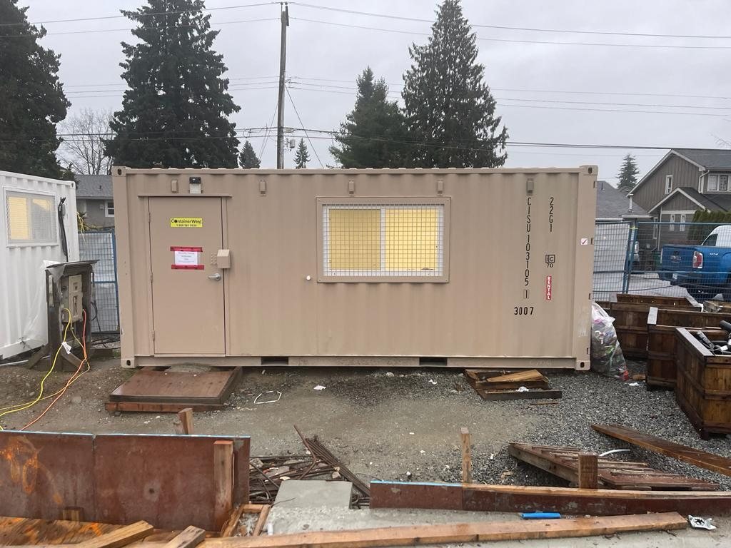 Portable construction office beside a muddy work area and residential building frames.