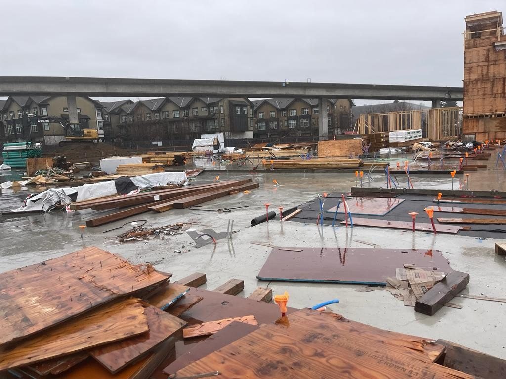 Concrete floor with plywood sheets, service lines and framing materials staged nearby.