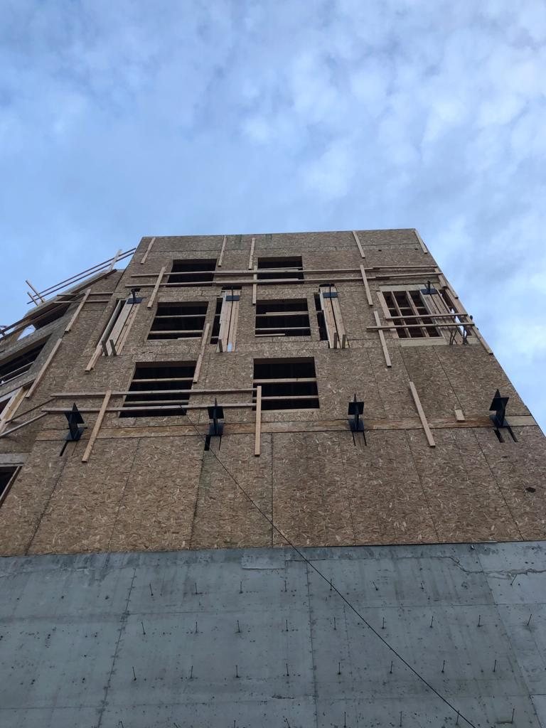 Upward view of a tall wood-framed exterior wall with multiple window openings.