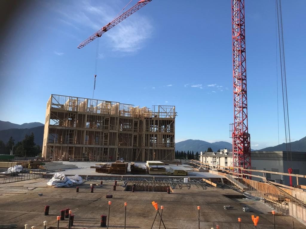 Construction crane beside a multi-storey wood-framed building with open wall framing.