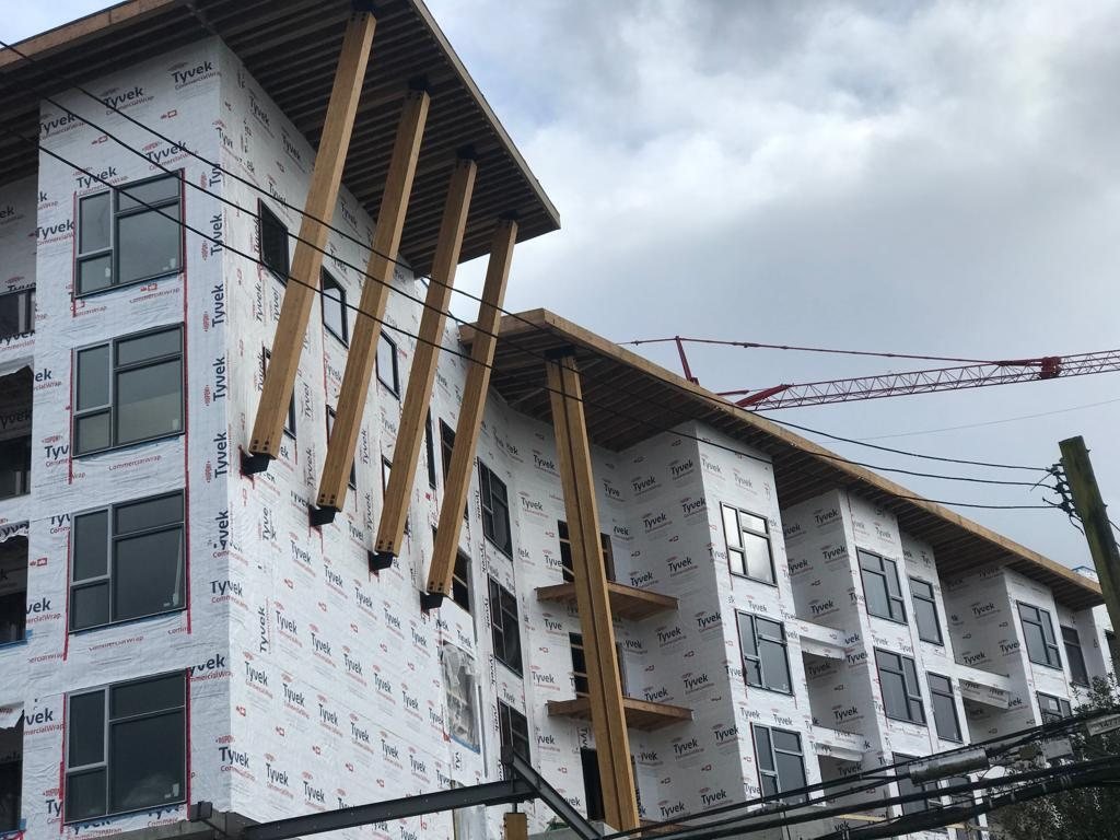 Projecting timber canopy supports beside windows on a wrapped multi-storey building.